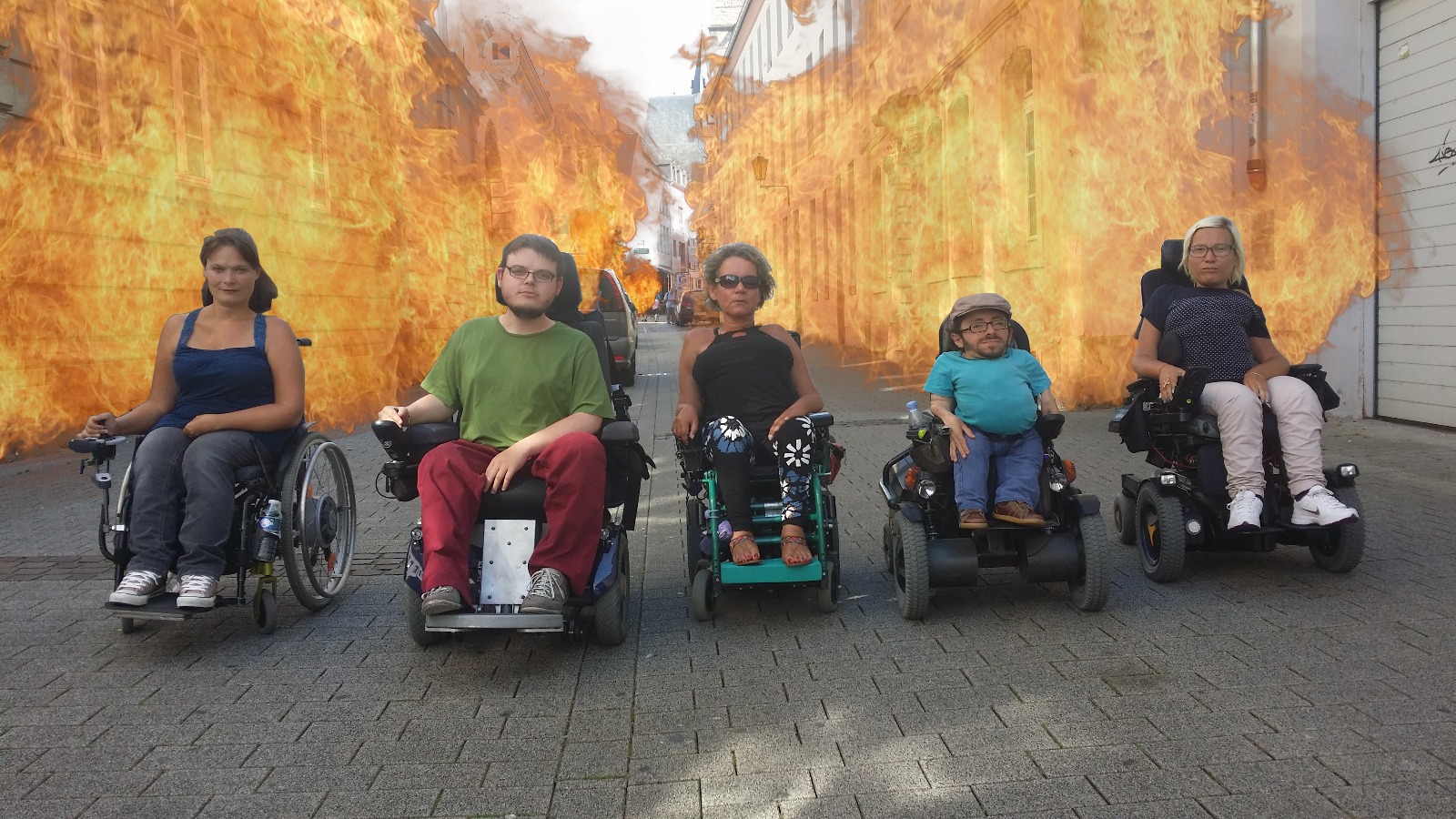 Fünf Rollstuhlfahrer nebeneinander. In der Mitte Corina Zolle. Alle mit ernster Miene. Dahinter gephotoshoppte Flammen.