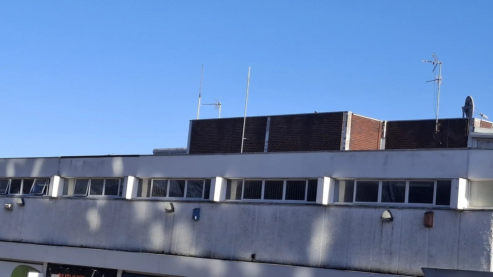 Blue sky with a white building in the foreground with a brick building in the background with street lights on the right