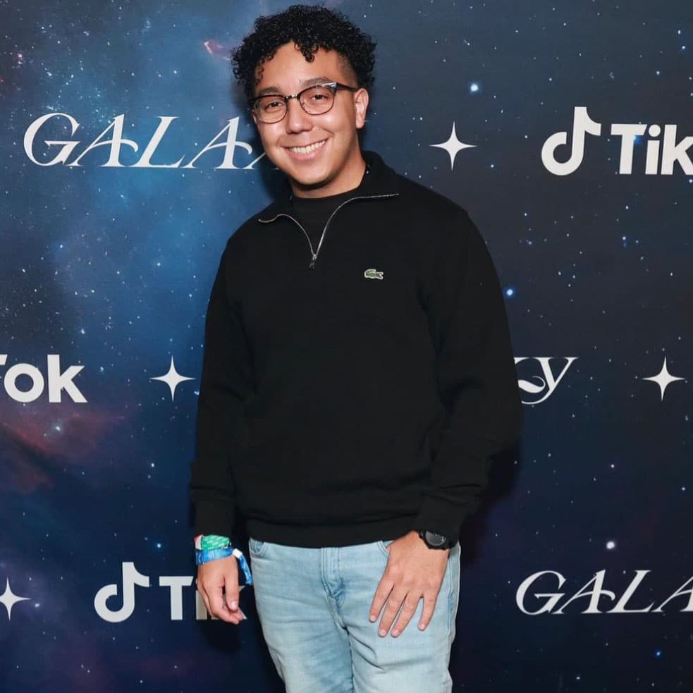 A Salvadorian and Black streamer, with dark curly hair, wearing a black hoodie and jeans.