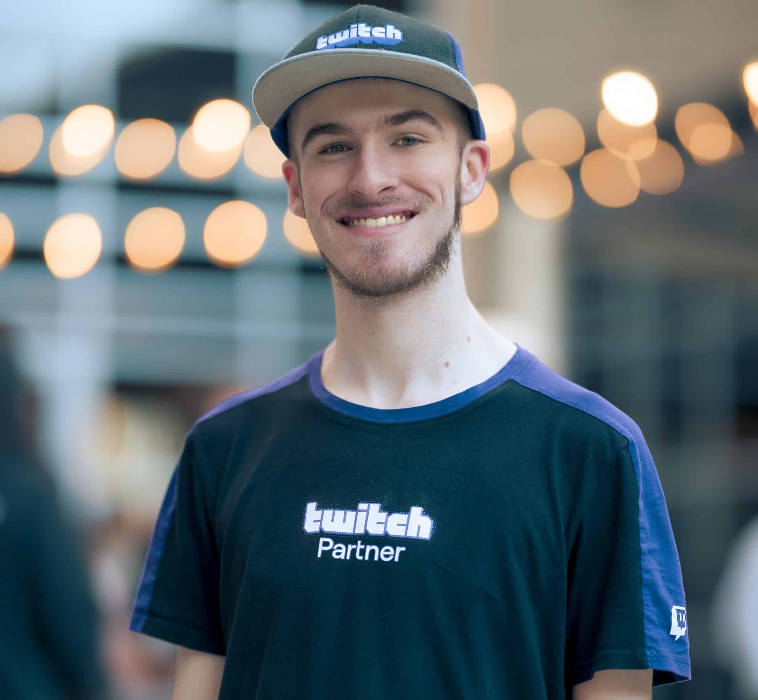 caucation man with a beard. Looking at the camera, wearing a black shirt and baseball hat that says Twitch Partner on it.
