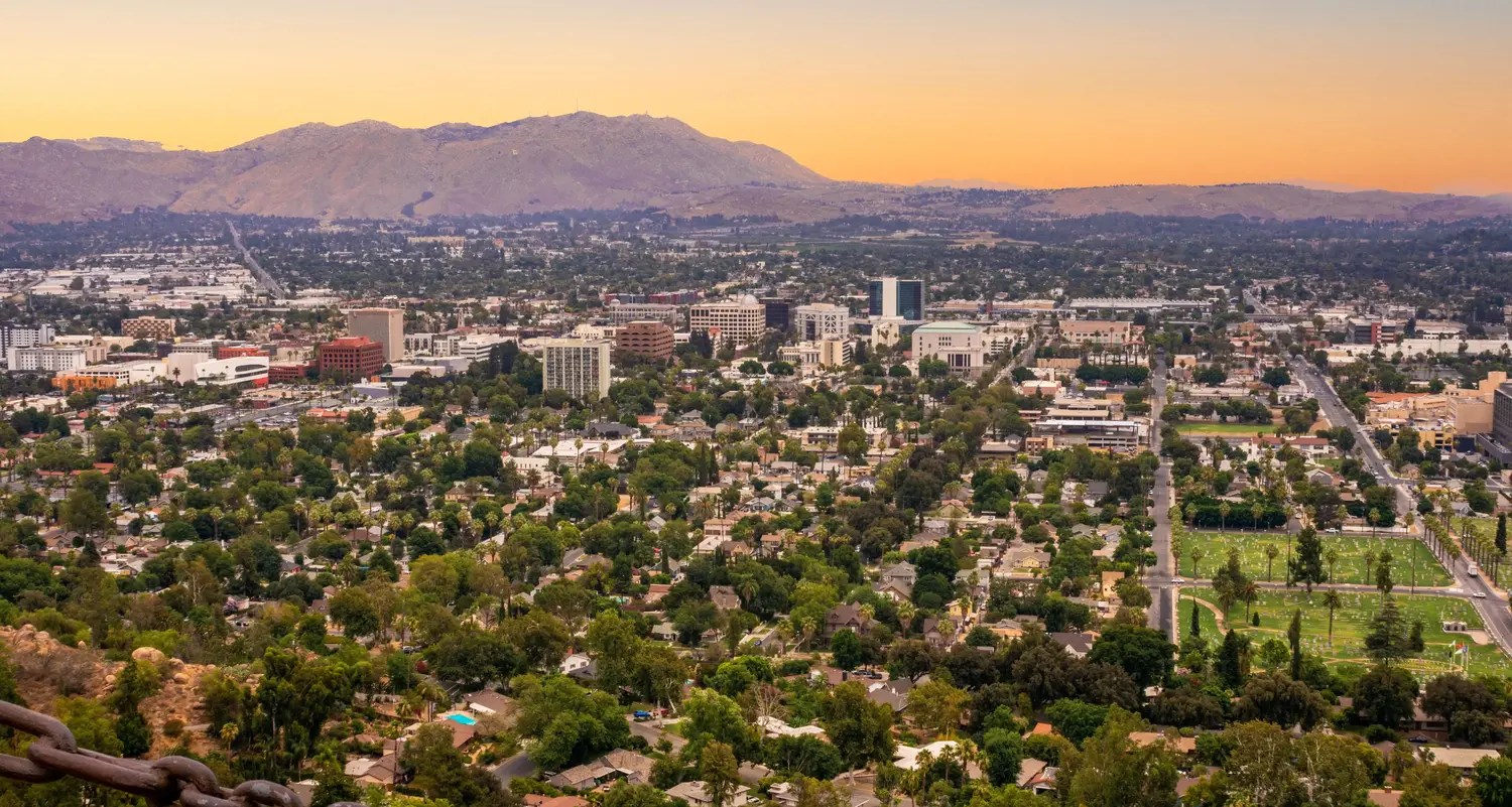 Aerial View Of A City Skyline And Residential Neighborhoods With Mountains In The Background At Sunset