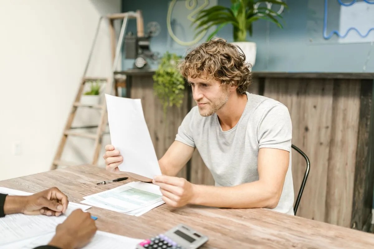 Person Reviewing Paperwork Across A Desk During A Consultation