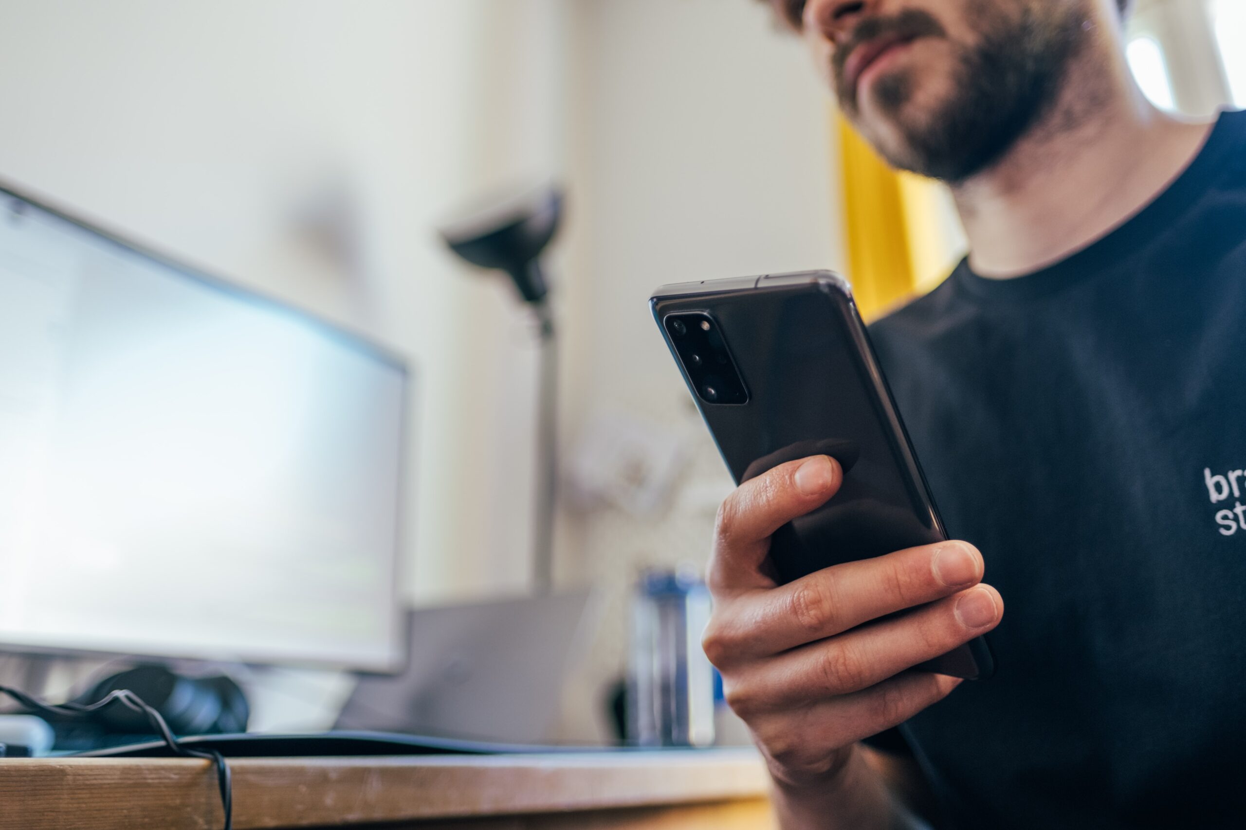 Mann sitzt am Schreibtisch und hält Smartphone in seiner rechten Hand.