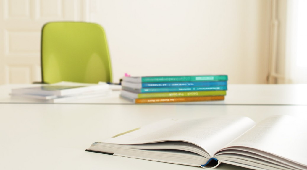 Tisch mit aufgeschlagenem Lehrmittel, weitere aufgestapelte Bücher im Hintergrund auf dem Tisch