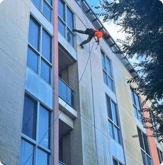 Rope access technician pressure cleaning a building