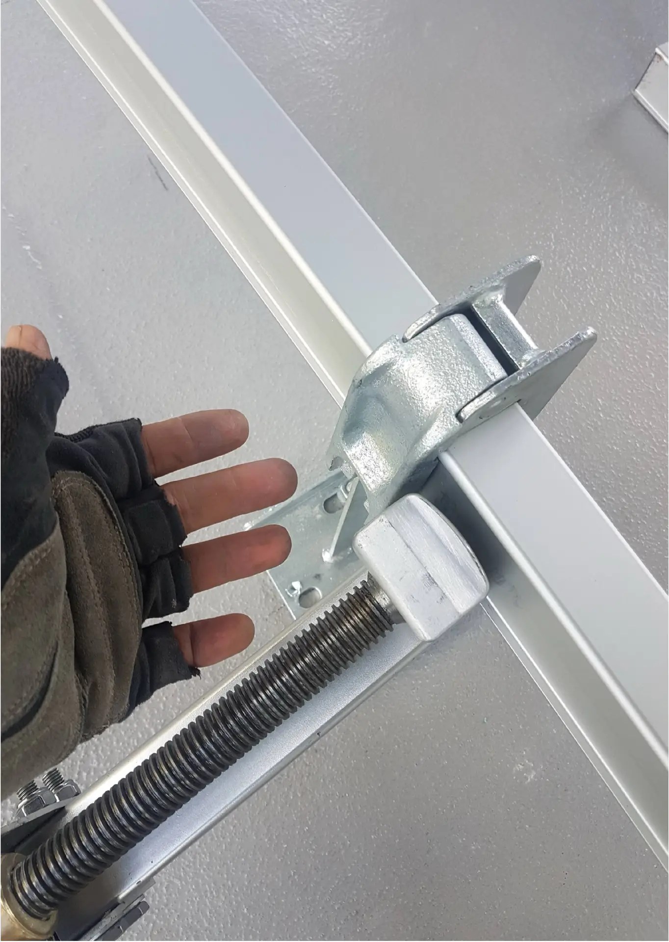 Gloved hand near a metal clamping mechanism with a threaded rod and bracket fixed to a metal beam.