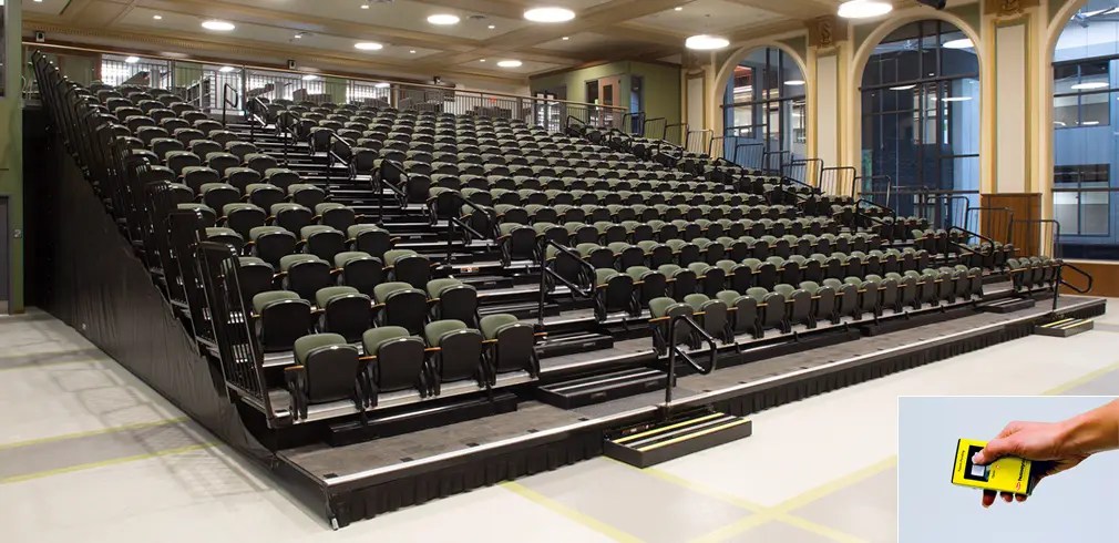 Large retractable auditorium seating with black and green chairs, shown with remote control for operation.