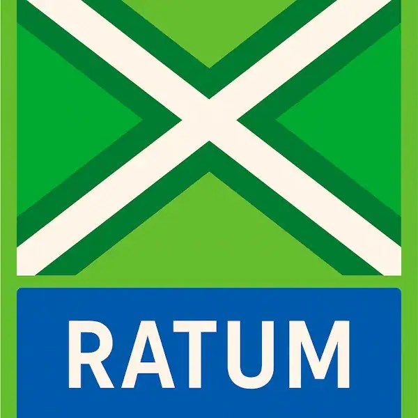 Plaatsnaambord met de tekst "RATUM" in witte hoofdletters op een blauwe balk. Daarboven een vlag met lichtgroene achtergrond, een helder wit St. Andrieskruis gecentreerd in een donkergroen kruispatroon — conform het originele vlagontwerp van de Achterhoek.
