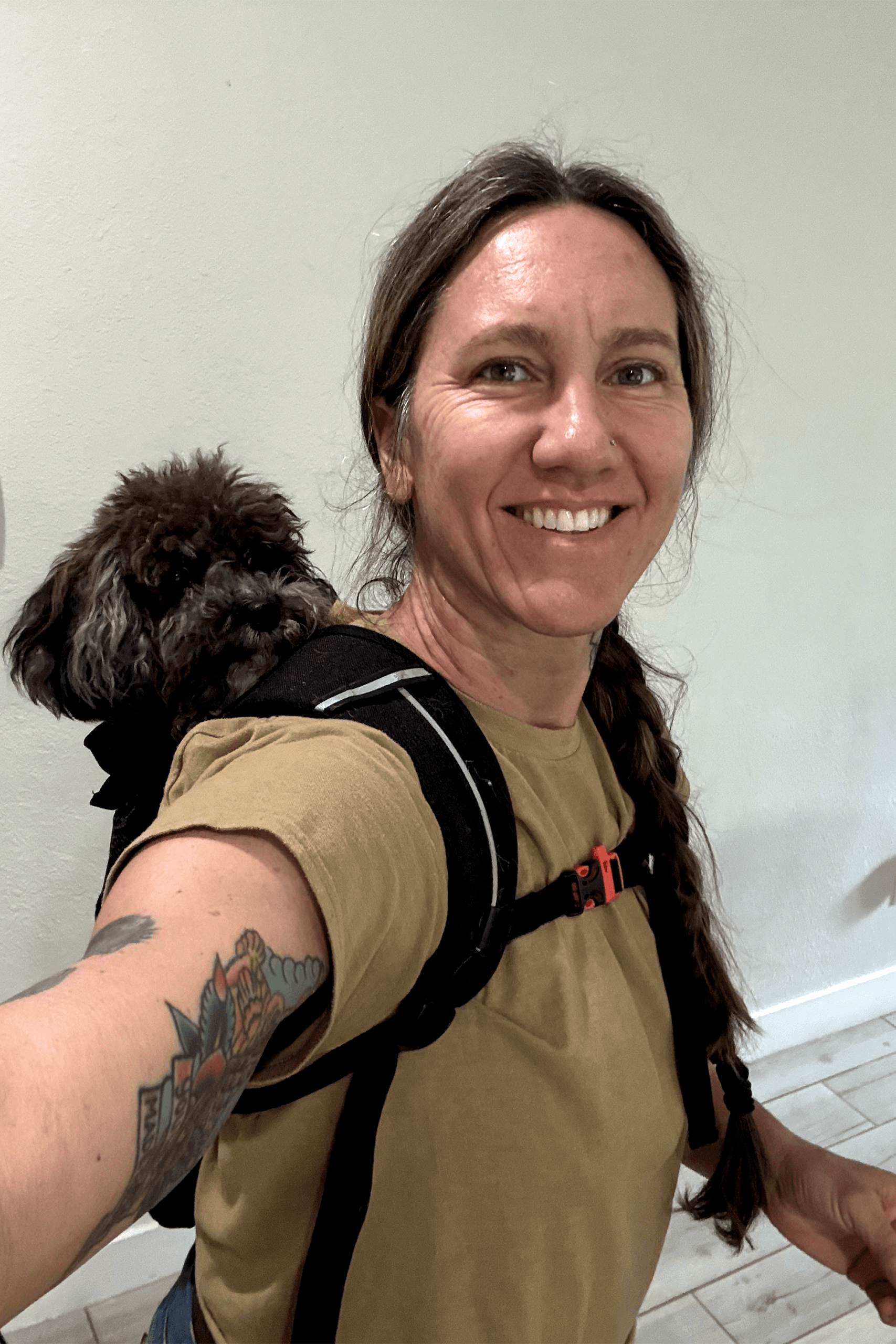 Woman smiling in a selfie with a small dog carried in a backpack.
