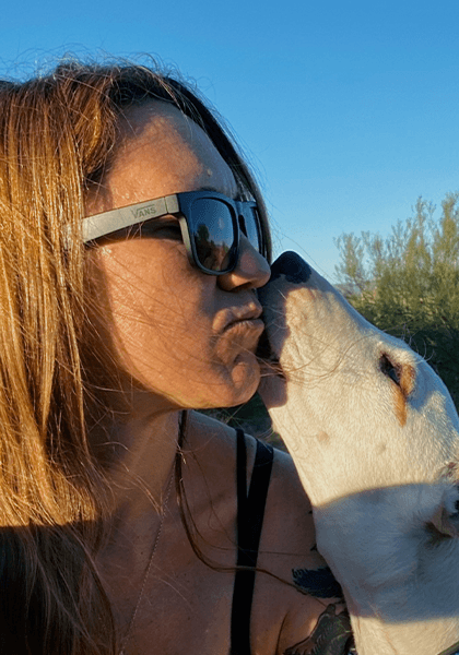 Woman getting a kiss from a white dog outdoors.