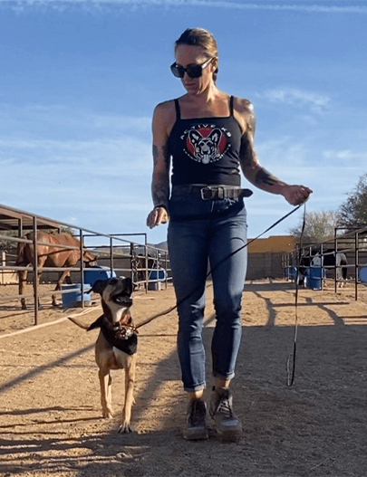 A woman walks her dog through a horse ranch.