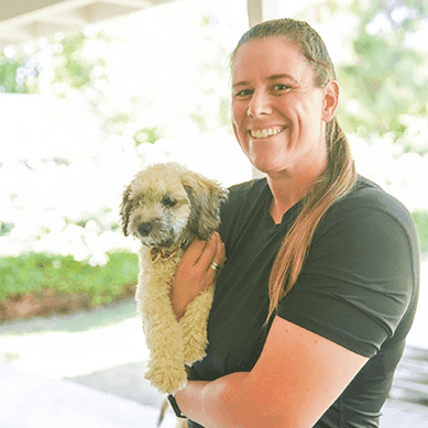 A woman smiling while holding a small dog outdoors.