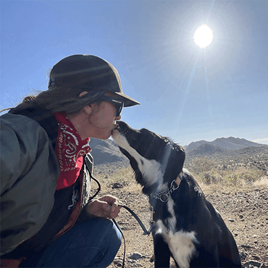 A woman sharing a kiss with her dog in the mountains.