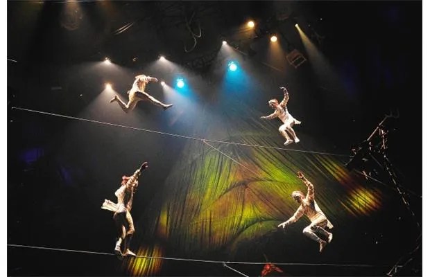 A group of acrobats performing on a tightrope under dramatic lighting in a circus setting.