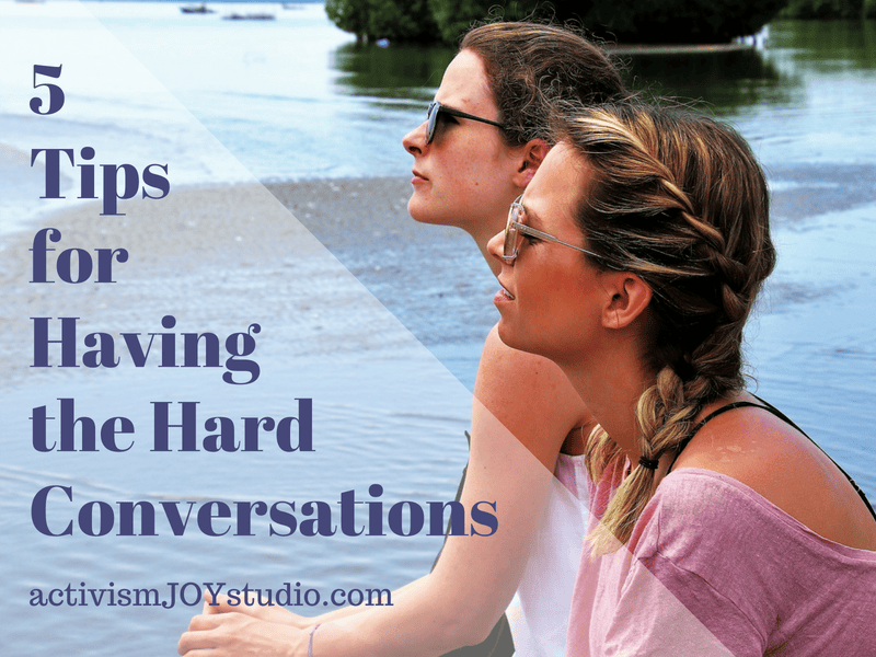 two white women sit and have a conversation while they look out over the water