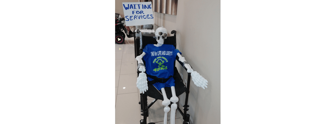 Skeleton on a wheelchair with a sign that reads "Waiting for services"