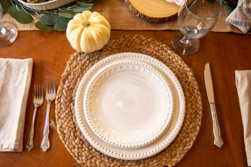 Basic, informal yet simple thanksgiving table setting using white everyday dishes, glass water cups, woven chargers, real utensils and linen napkins.