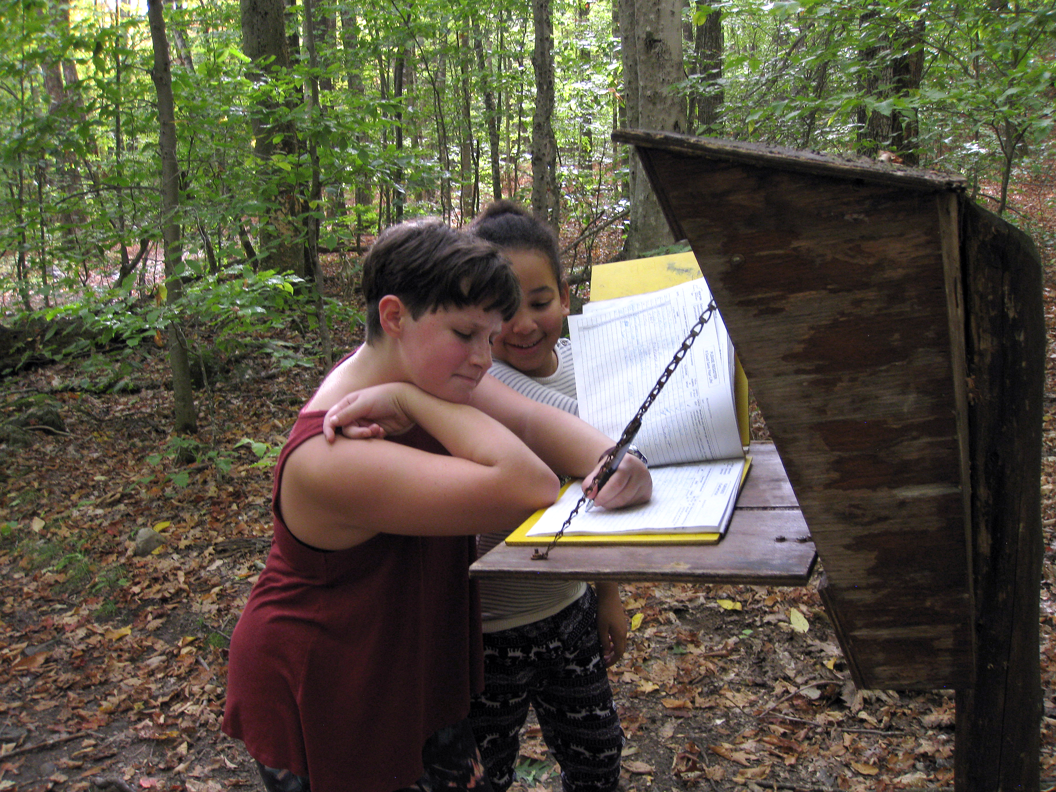 Brigid studies the trailhead logbook as Eniola looks on. She is checking the "out" box as we head for the car.