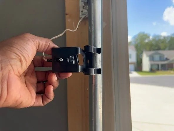 Hand adjusting a garage door safety sensor mounted on a track bracket