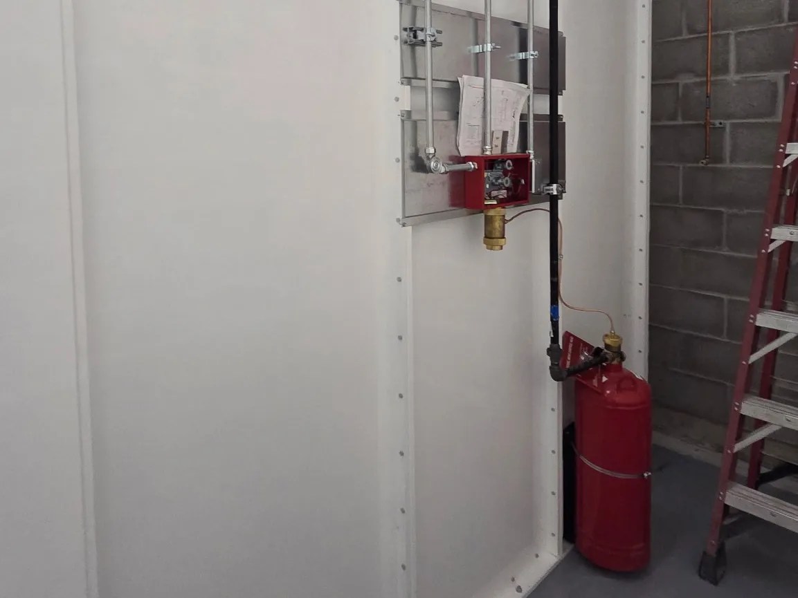 Exterior side wall of an AEL Mega Series enclosure with a fire suppression cylinder and piping