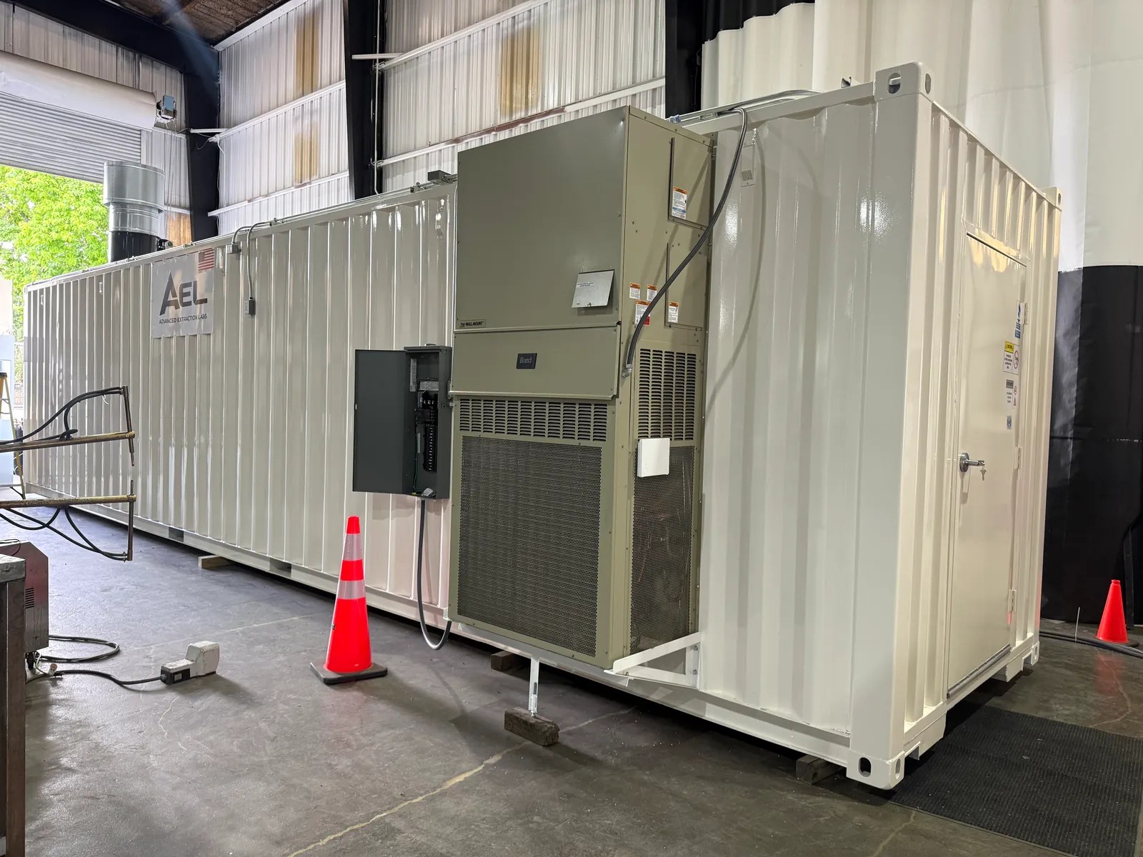 White AEL modular container with a wall-mounted HVAC unit and electrical disconnect in a shop