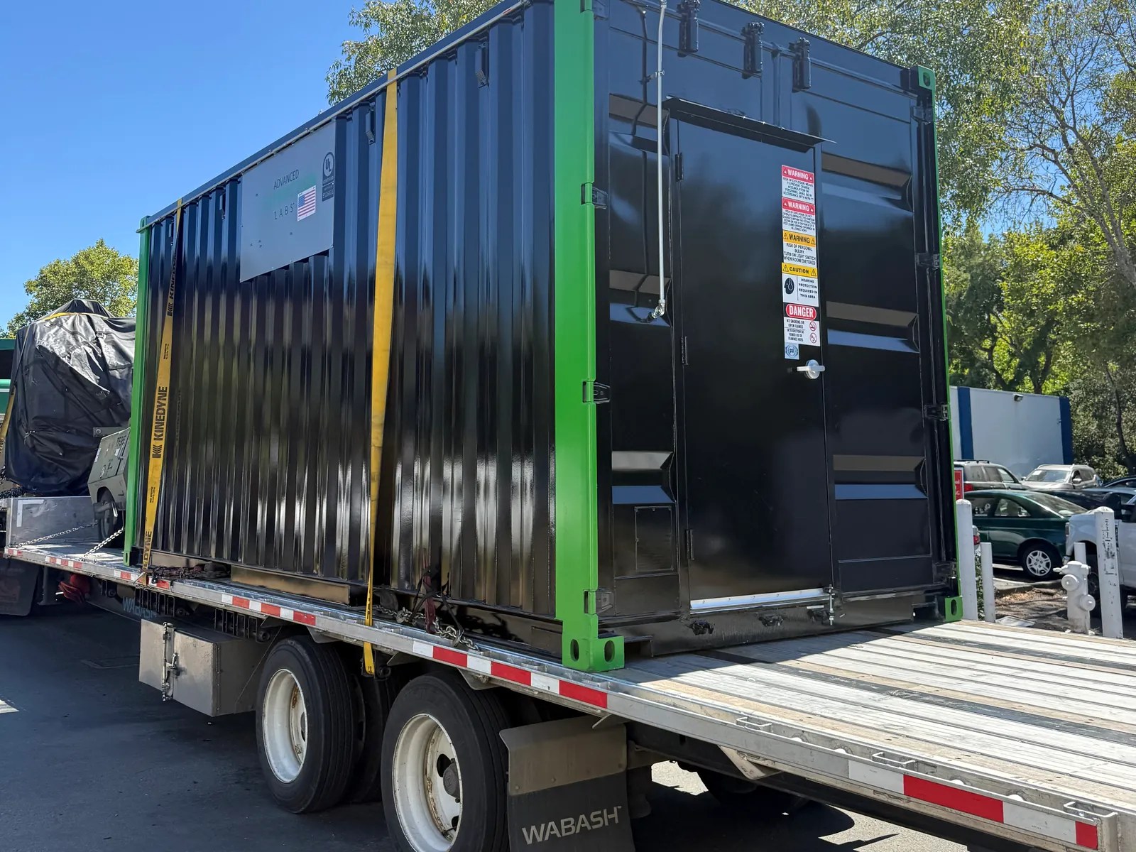 Black modular container with green corner trim on a flatbed trailer against a blue sky
