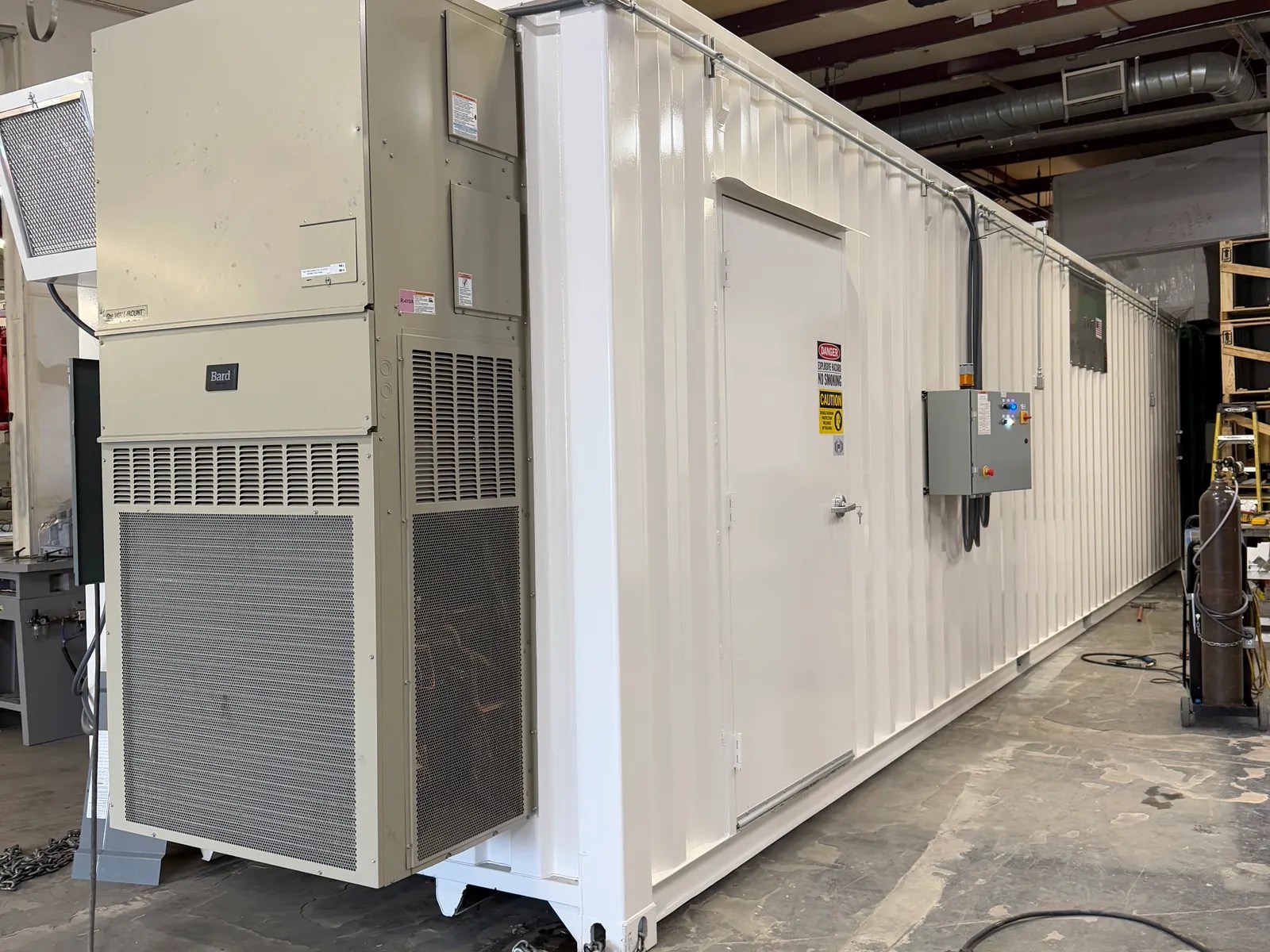 White modular container with a large end-mounted HVAC unit inside a fabrication shop