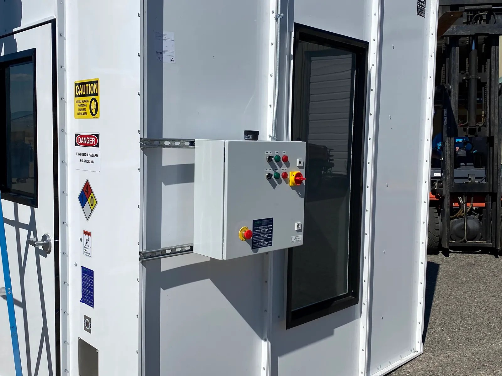White modular enclosure with windows, safety placards and an exterior control panel