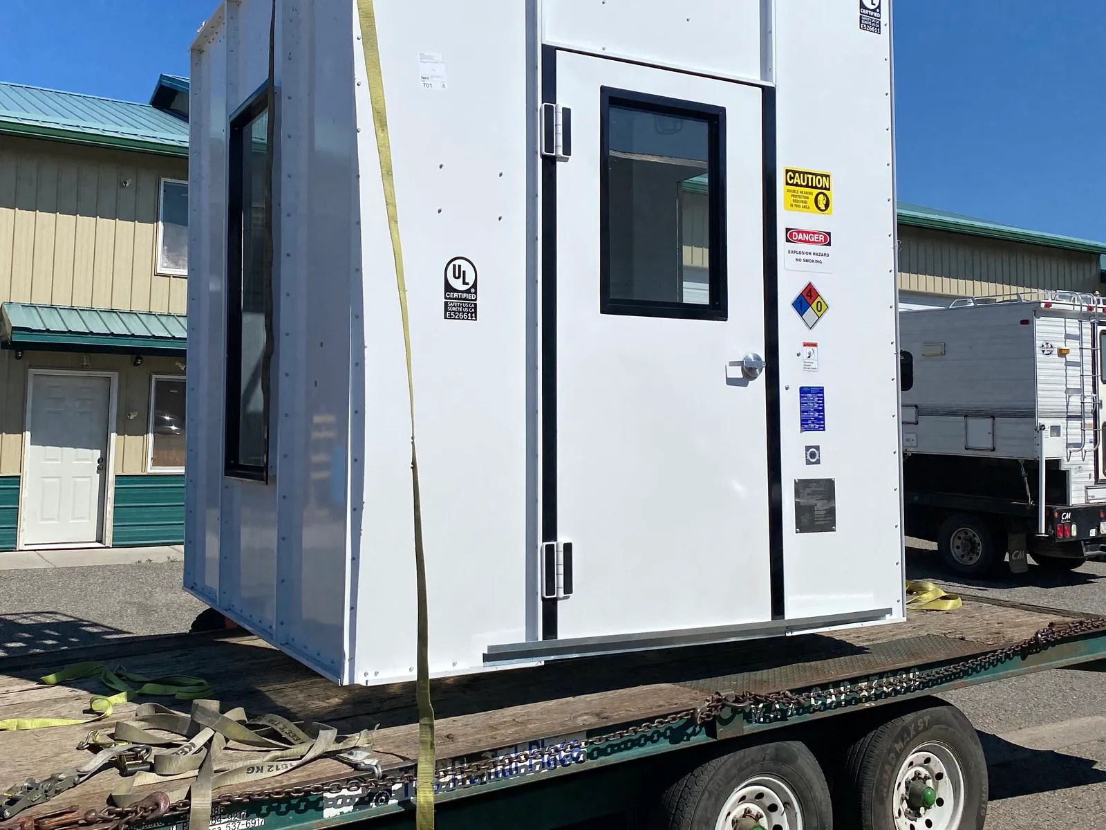 White modular enclosure strapped to a trailer for delivery under a blue sky