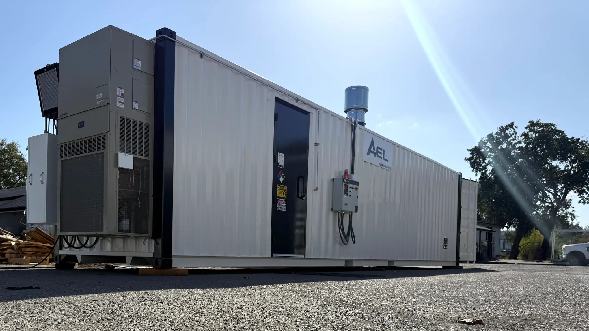 AEL modular enclosure with end-mounted HVAC and an exterior control panel, on a gravel lot under a clear sky