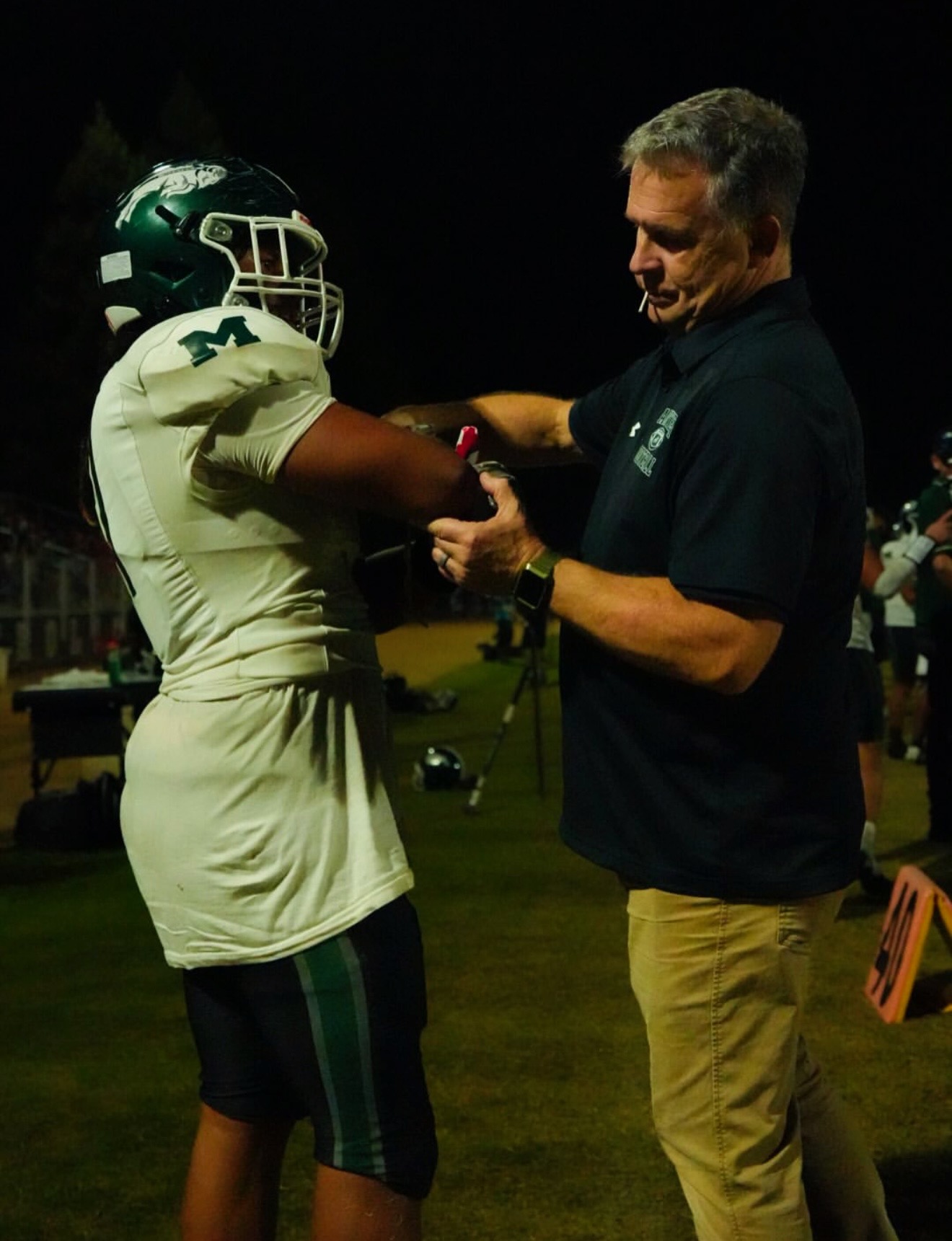 Athletic trainer performing on-field physical therapy for football player during a game.
