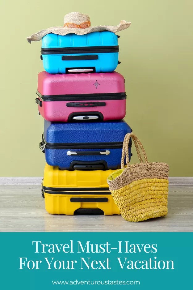 Travel Must-Haves for your next vacation from adventuroustastes.com 
Stack of multi-colored suitcases with a straw bag and a straw hat.