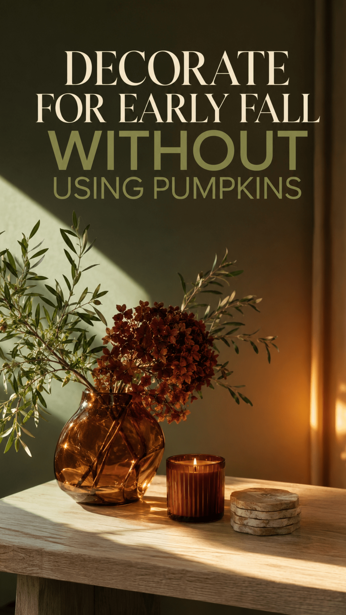 Pumpkin-free early fall coffee table decor with an amber glass vase, olive branches, dried burgundy hydrangeas, rust-colored candle, and stone coasters.
