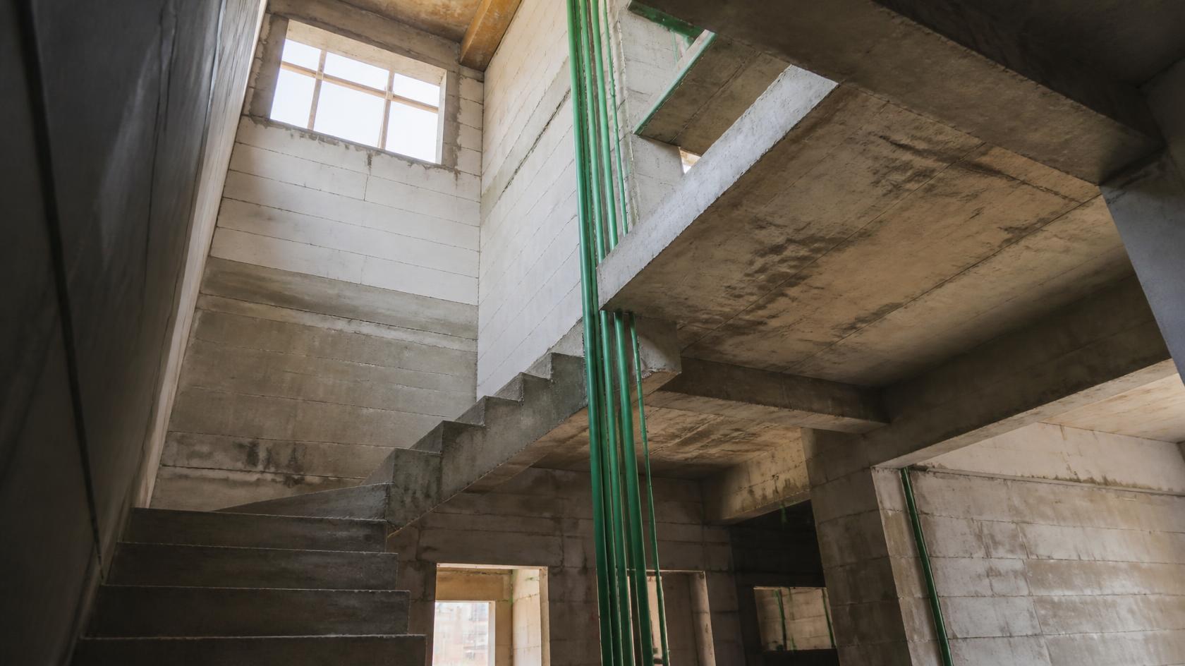 Exposed green PP-R water vertical supply pipes running up through the concrete stairwell of a multi-storey house under construction.