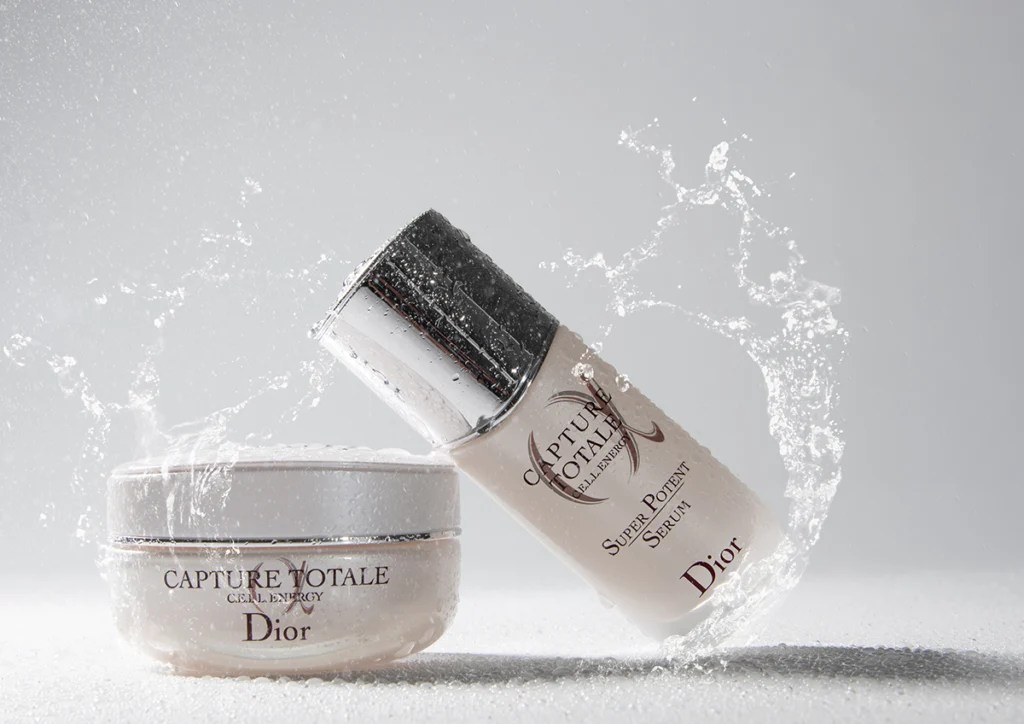 Dior Cremedose, daran angelehnt eine Dior Serumflasche mit Wasser bespritzt