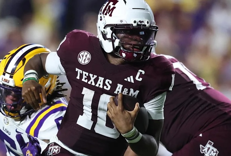 Texas A&M football player wearing maroon jersey with 'C' for captain, running with the ball while being pursued by an opponent in a game.