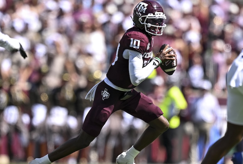 A football player in maroon and white uniform, number 10, prepares to throw the ball during a game. The background shows a cheering crowd in a stadium.