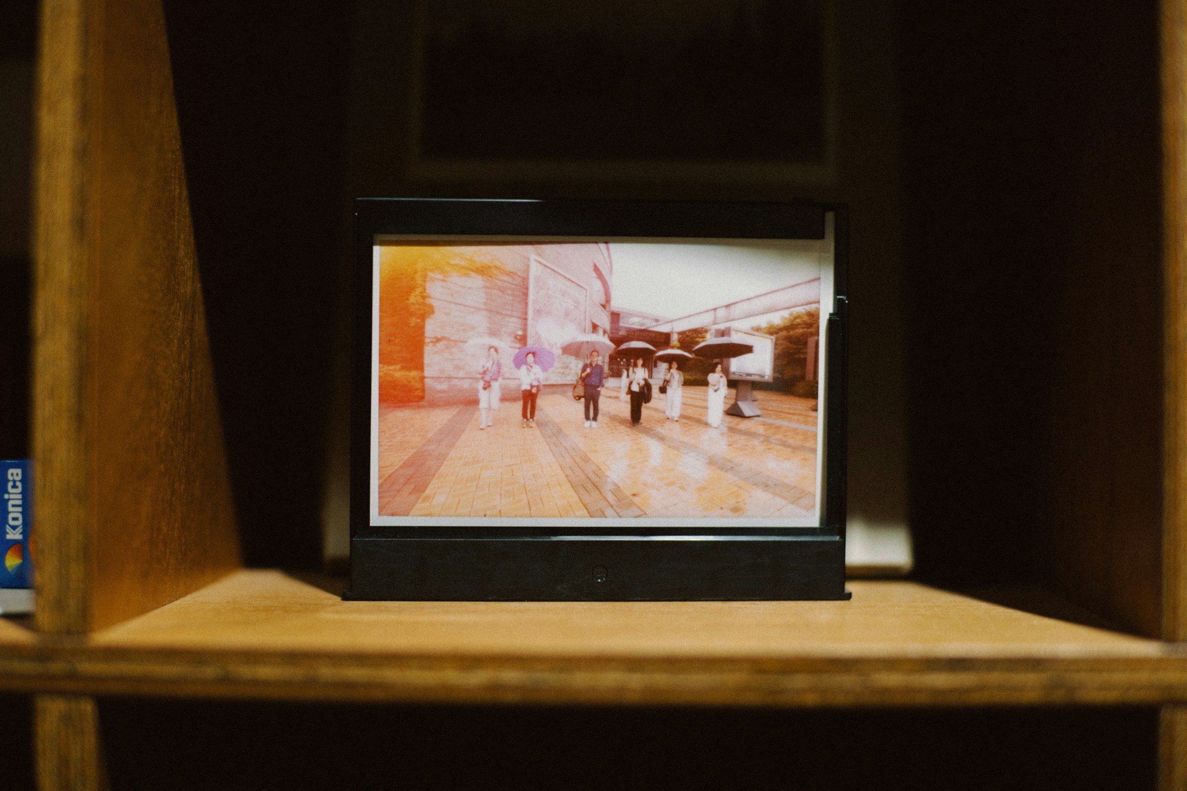 A black photo frame on a wooden shelf showing a street scene of people with umbrellas