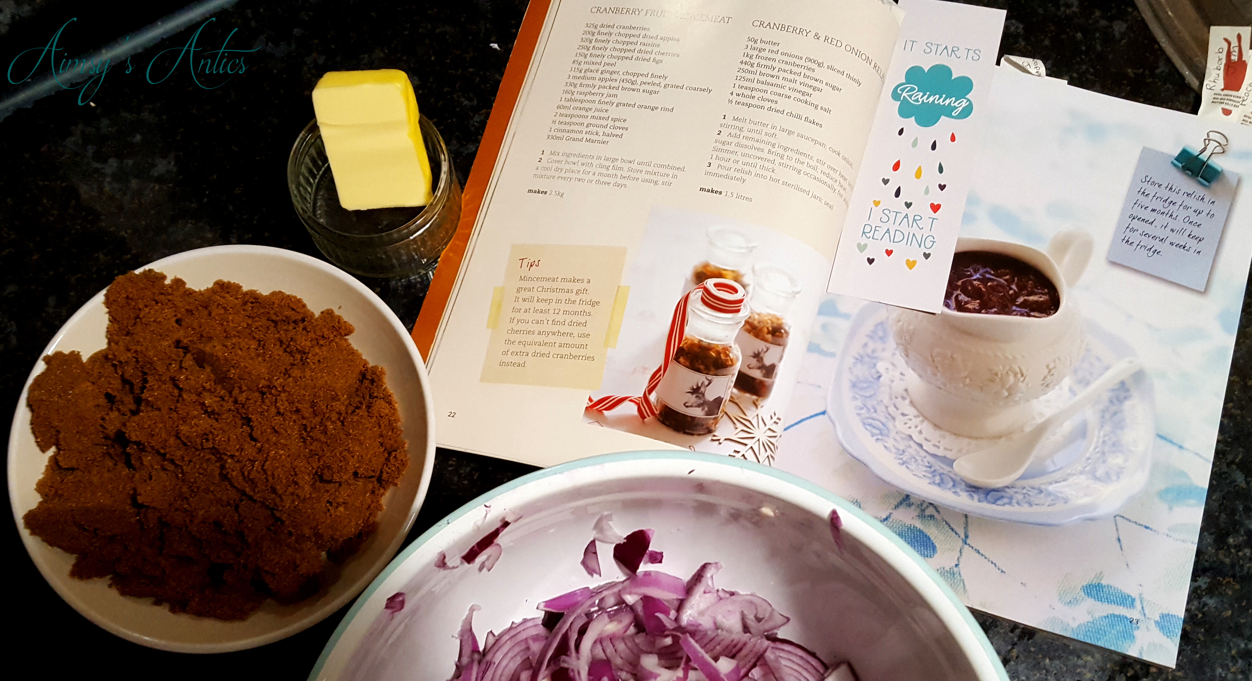 Image of a recipe book (Australian Women's weekly) with a bookmark, butter in a small dish, a bowl of sugar and a bowl of sliced red onions.