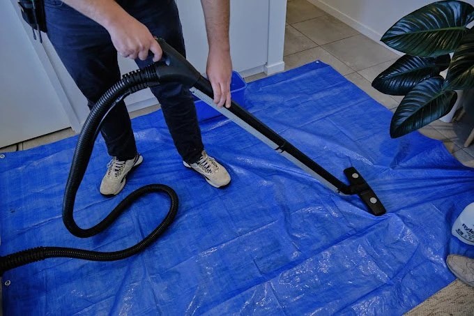 Person vacuuming a blue tarp on the floor inside a house.