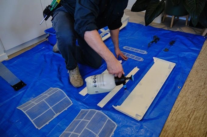 Person kneeling on a blue tarp, using a glue gun to install solar panels and other components onto a flat surface.