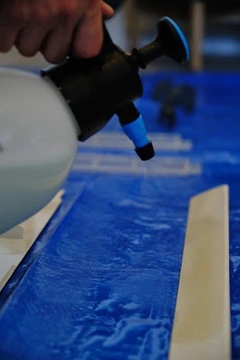 A person applying a white sealant or adhesive along the edge of a blue surface using a black nozzle tool.