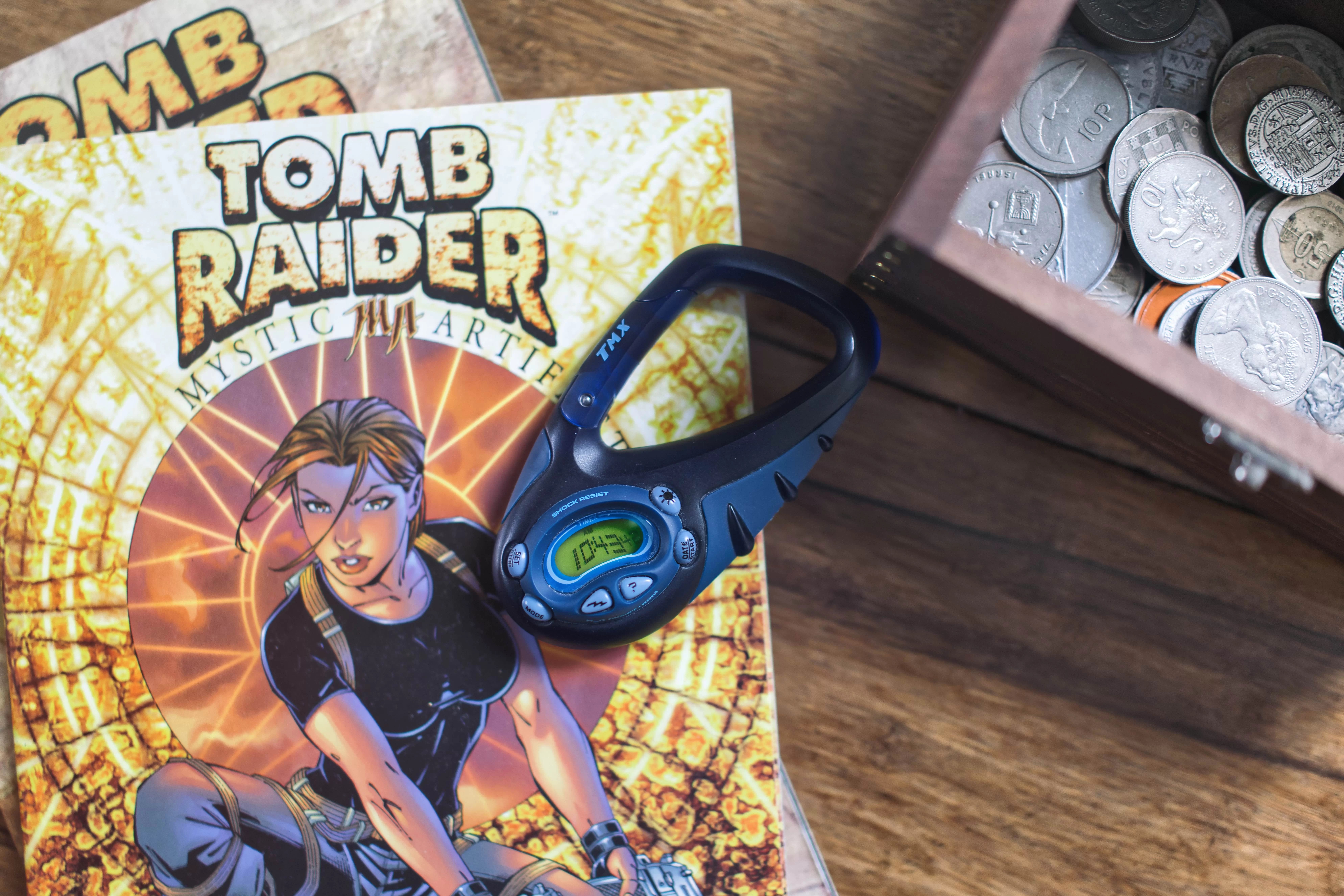 Blue TMX watch on a stack of Tomb Raider comics and the corner of a treasure chest with coins to its right