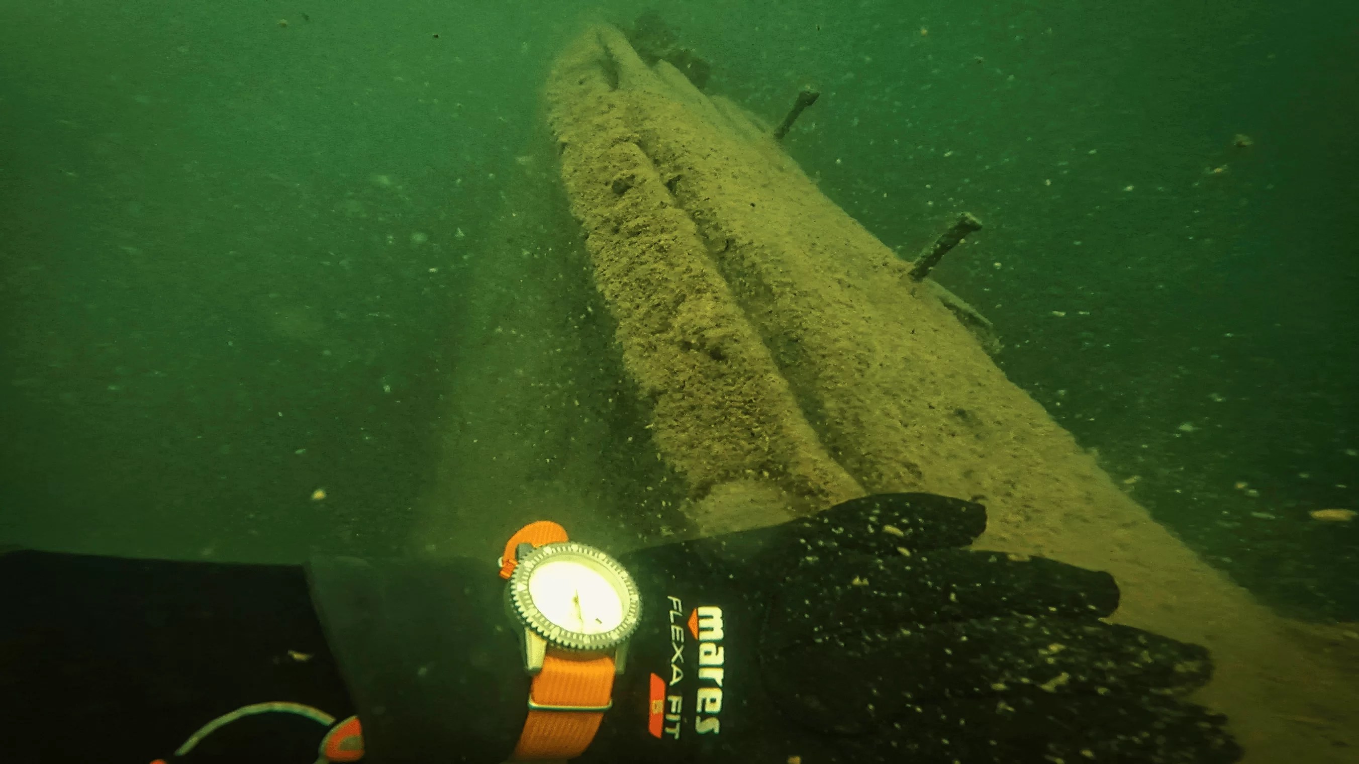 White dial ARES diver-1 on wrist of AJ at about 25ft underwater, with his hand on what remains of the hull of the ship. Green water all around and debris in the water from putting hand on hull