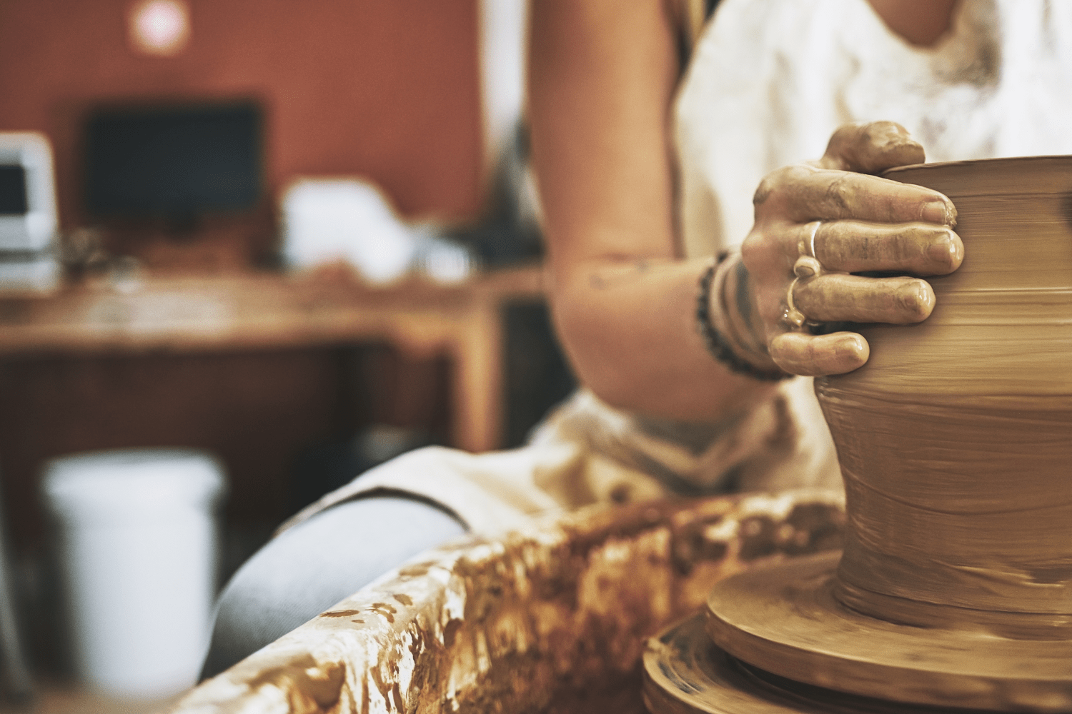 A woman in a pottery studio in full action on the wheel, shaping clay into a vase.