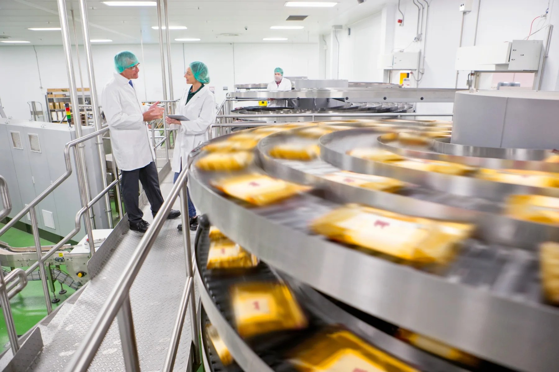 Two food manufacturing employees discussing operations beside an automated packaging conveyor.