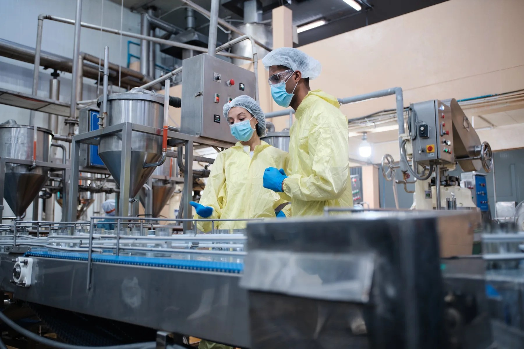 Two food processing employees wearing protective clothing reviewing equipment on a production line.