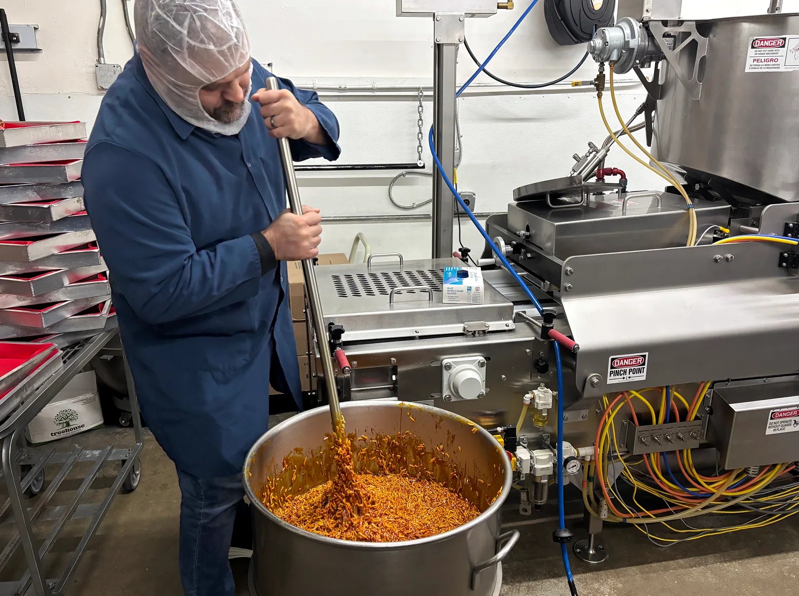 Team member in protective clothing stirring ingredients in a large metal bowl beside production equipment.