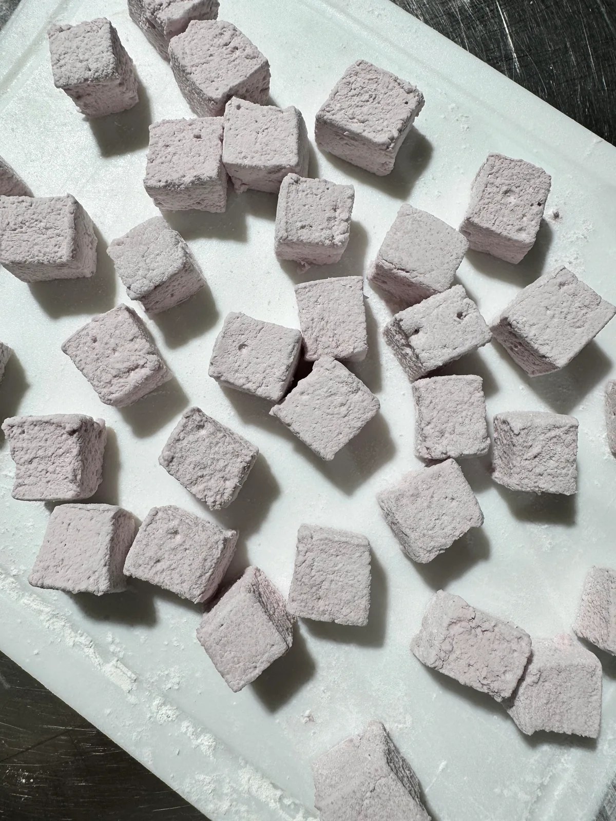 Pale powder-coated food cubes on a white cutting board beside a stainless steel work surface.