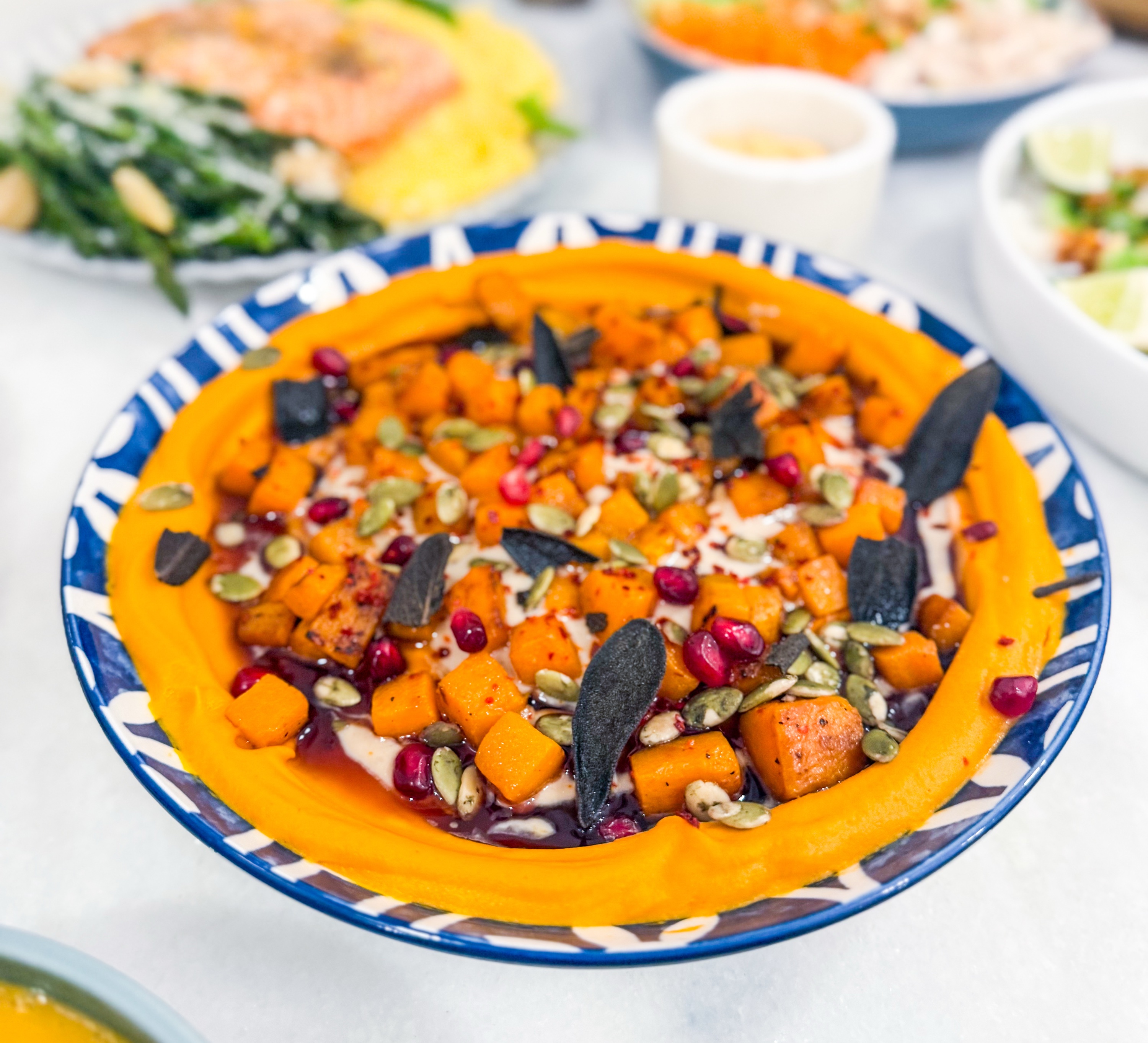 Honeynut Squash Hummus - Roasted honeynut squash hummus topped with lemon-tahini, pepitas, pomegranate molasses, fresh pomegranate seeds, and crispy sage served with pita